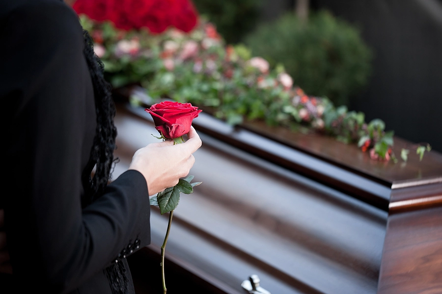 Person holding rose in front of coffin