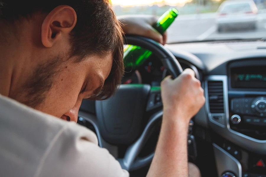 Person-sleeping-against-steering-wheel-with-beer-bottle-in-hand